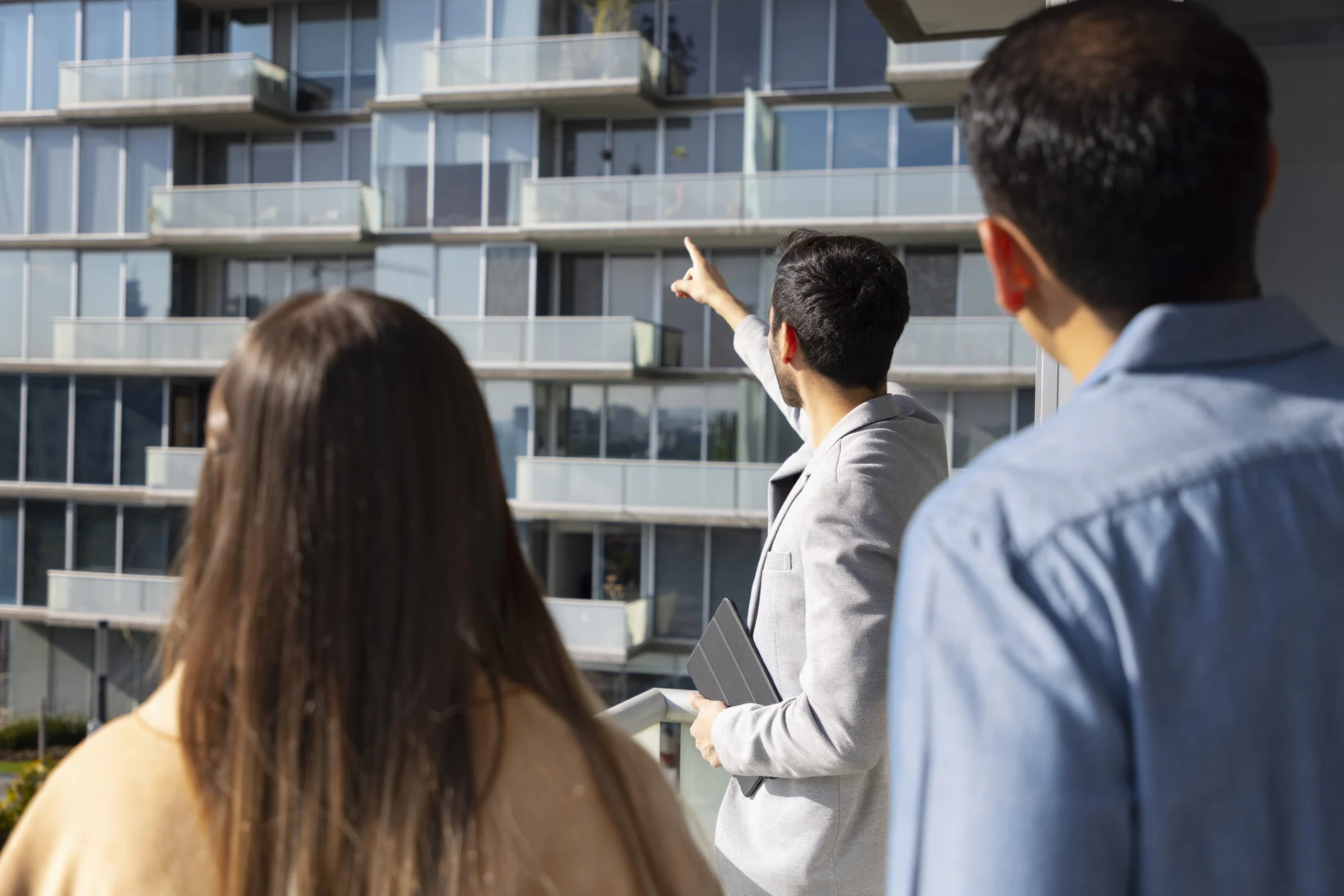 Real estate agent showing a young couple available units in a modern glass-fronted condominium building in Delray Beach, Florida.